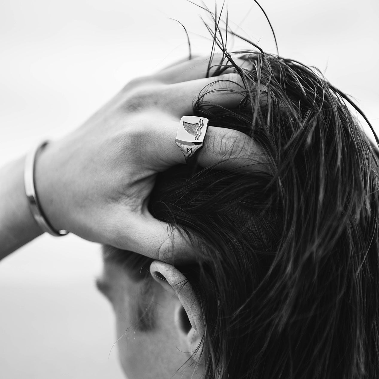 Hands calming through hair while wearing titanium signet ring with an engraved shark fin, and a titanium bracelet.