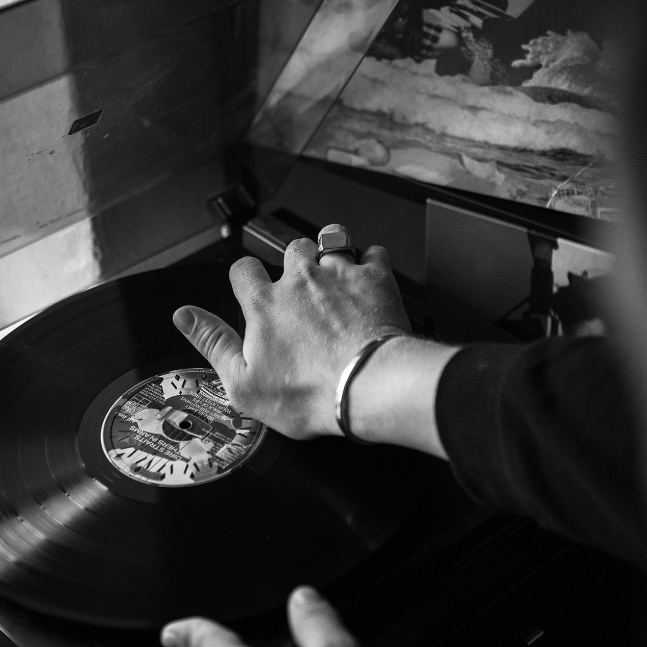 Hand and arm reaching for a record player while wearing a titanium ring and bracelet.