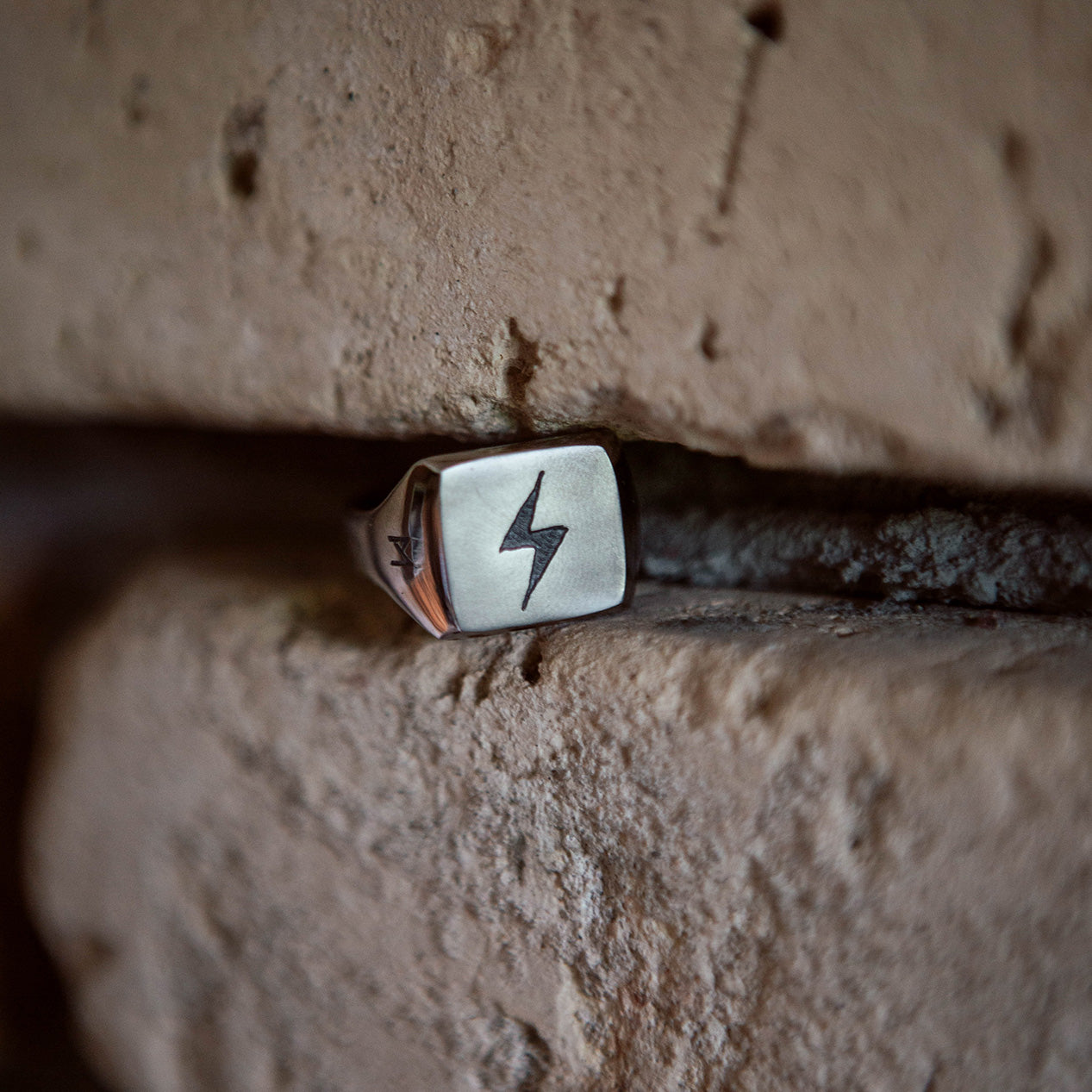 Titanium signet ring with an engraved lightning bolt. The ring is held between two bricks.