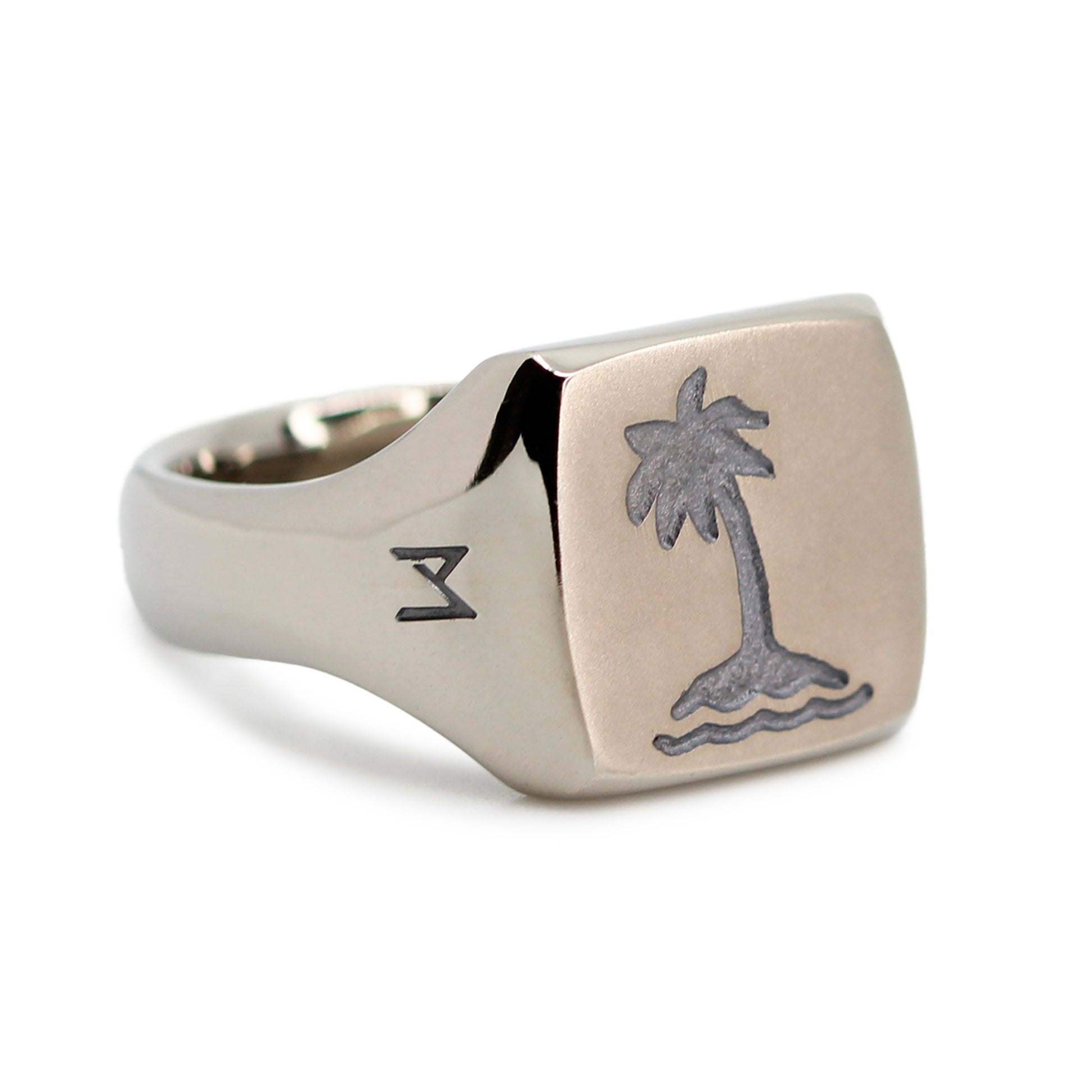 Single silver-colored titanium signet ring, 15x15 mm wide surface with an engraved palm tree. Image shows corner view of the ring
