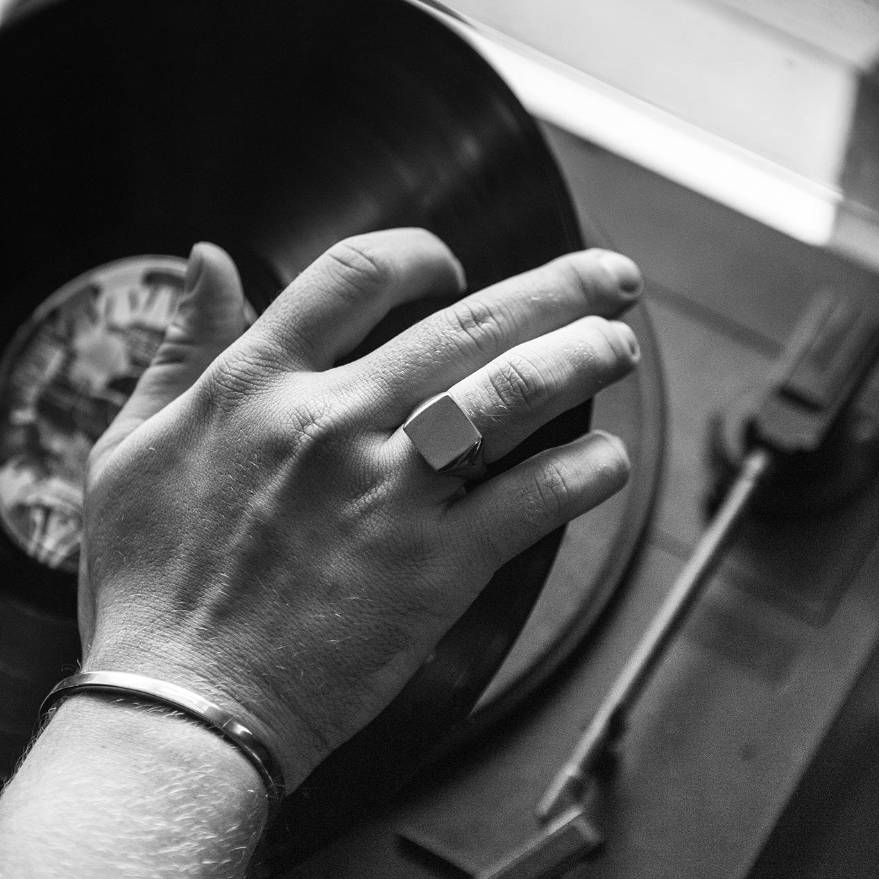 hand and wrist wearing a titanium signet ring and a titanium bracelet, reach for a record player.