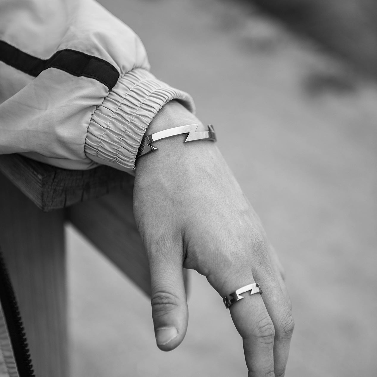 Hand and arm wearing titanium ring and bangle, both with the same matching zig zag pattern leaning on a wooden railing.