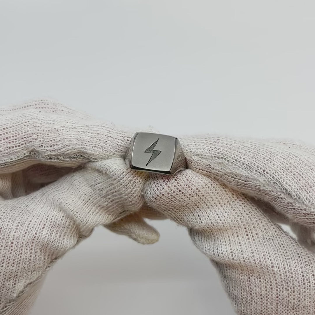 Showing single silver-colored titanium signet ring, 15x15 mm wide surface with an engraved lightning bolt from all angles.