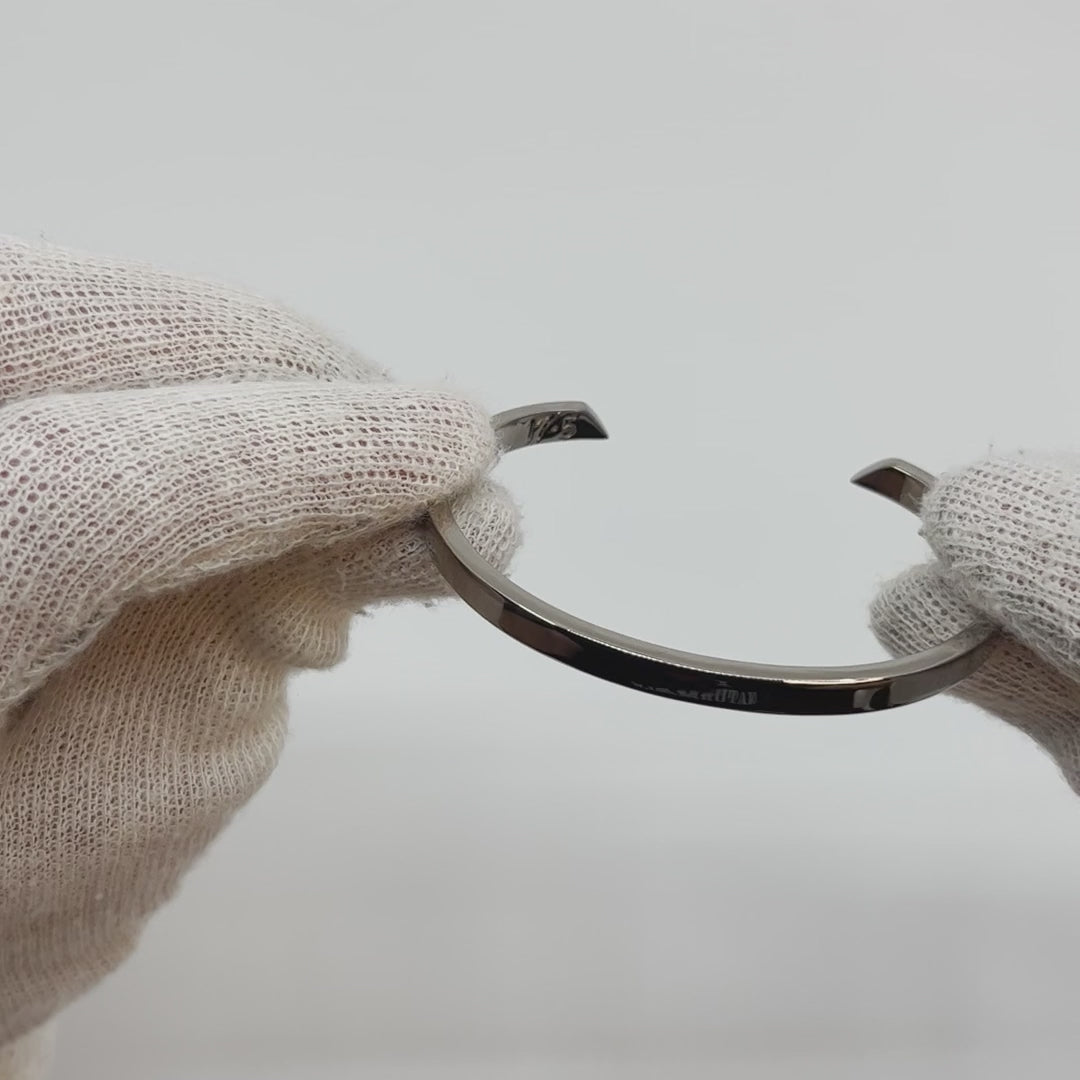 Video showing silver-colored titanium bangle, 5 mm wide, being rotated to show all sides. Background is plain.